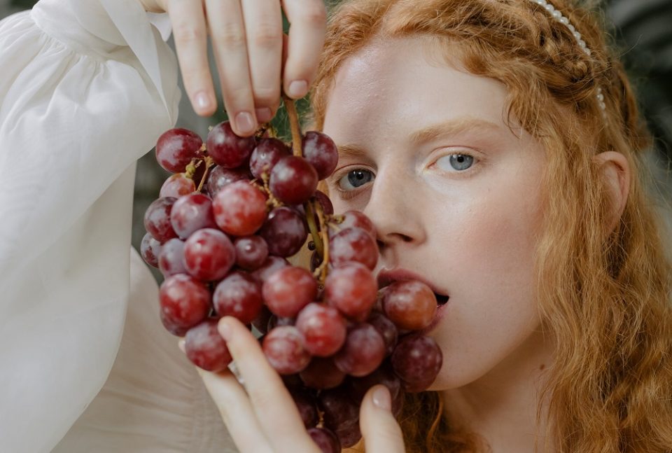 Donna con capelli rossi tiene un grappolo di uva rossa, frutto di stagione tipico dell’autunno