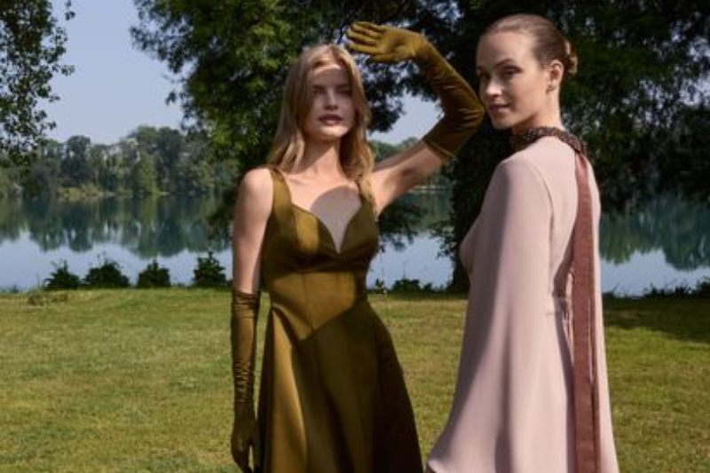 Due modelle sul prato, una in abito da sera verde e l'altra in abito rosa con spalline ricamate, per la campagna Emé Elegance