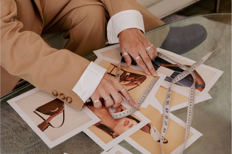 Moodboard creativo: processo di ispirazione per un fashion designer Mani che sfogliano fotografie di moda con metro da sarta, simbolo di creatività e lavoro nel fashion design