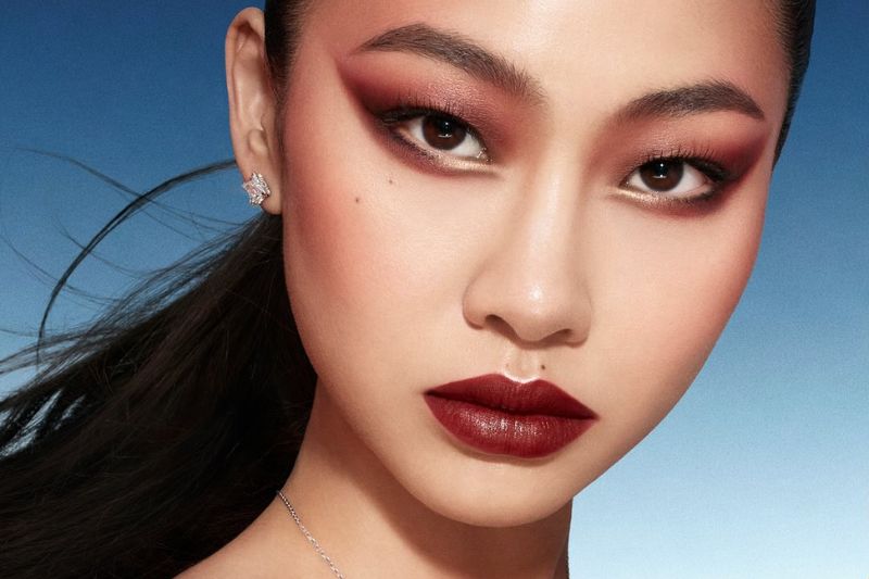 Un ritratto ravvicinato di Jung Hoyeon con un trucco occhi drammatico in tonalità bordeaux, labbra scure, e un orecchino di diamanti, per la campagna Louis Vuitton La Beauté.