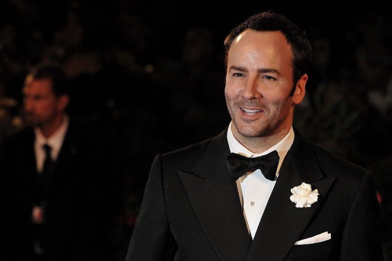 Tom Ford sorride sul tappeto rosso, indossa uno smoking nero con papillon e un fiore bianco all'occhiello