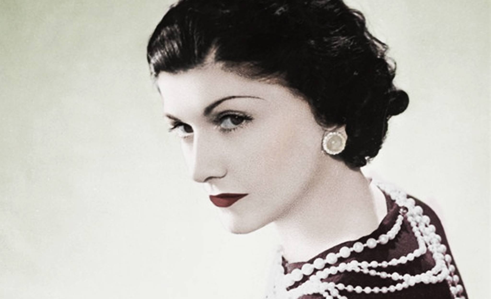 Gabrielle "Coco" Chanel in un ritratto d'epoca, con il suo iconico taglio di capelli scuro, un filo di perle e un rossetto scuro