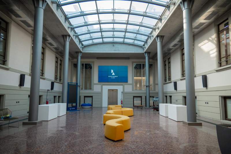 L'atrio della Domus Academy a Milano, con un grande schermo e un divano a forma di S di colore giallo