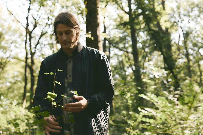 L'artista Julian Charrière tiene un rametto in mano, con un'espressione pensierosa, all'interno di un bosco