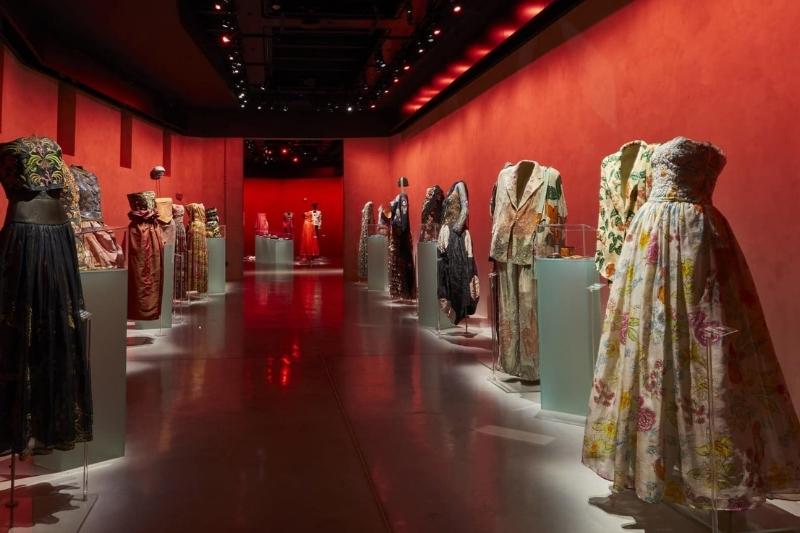 Interno di una mostra di abiti d’alta moda illuminati in una sala rossa per ApritiModa 2025, evento dedicato all’eccellenza del Made in Italy.
