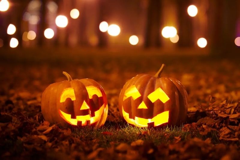Due zucche intagliate illuminate nella notte di Halloween 2025 tra foglie d’autunno e luci soffuse