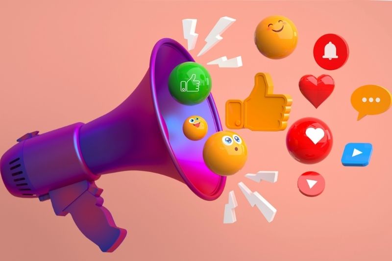 Megafono viola con icone 3D colorate dei social media — cuori, like, emoticon, notifiche e messaggi — su sfondo rosa, simbolo delle strategie di marketing locale online