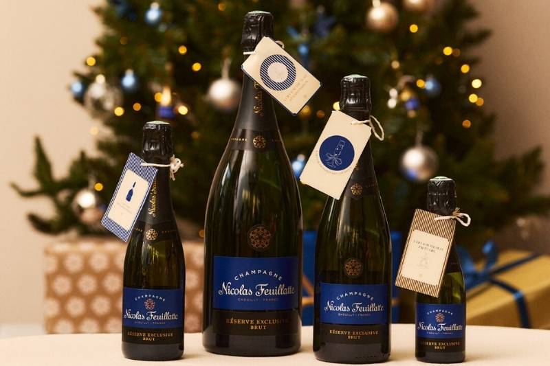 Bottiglie di champagne Nicolas Feuillatte Réserve Exclusive Brut in diverse formati davanti a un albero di Natale decorato