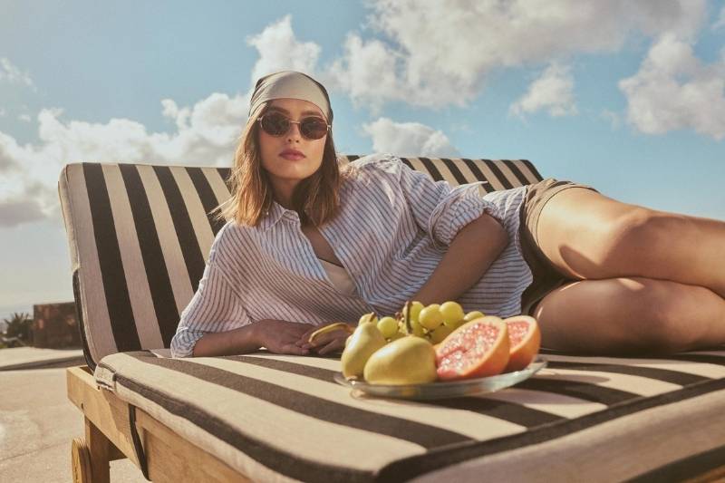 Modella Polo Club High Summer SS26 rilassata su lettino prendisole con camicia a righe e accessori estivi
