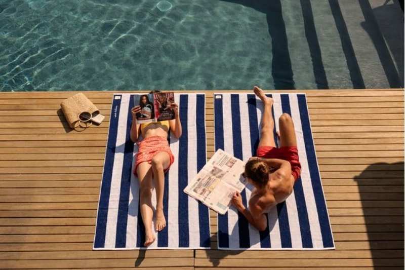 Due persone rilassate a bordo piscina sui teli mare a righe Dalfilo Portofino e Brezza in cotone 100% Made in Italy