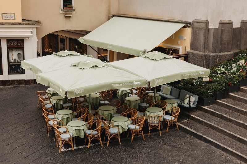 Dehors del Bar Tiberio di Capri personalizzato da Harmont & Blaine con ombrelloni, tavoli e arredi ispirati allo stile mediterraneo del brand