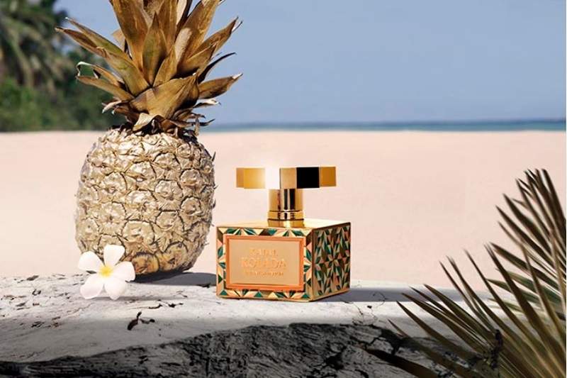 Flacone del profumo Kolada di Kajal Perfumes Paris ambientato su una spiaggia tropicale accanto a un ananas dorato