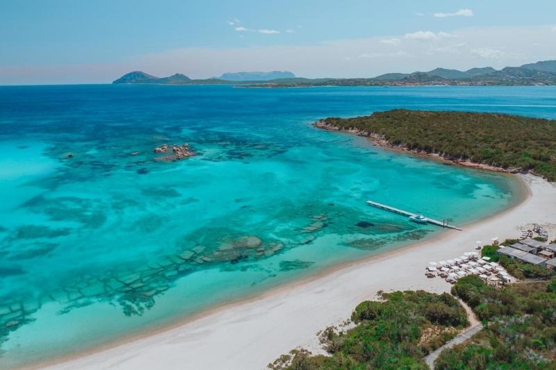 Veduta aerea di Nikki Beach Costa Smeralda con la spiaggia, il mare cristallino e il beach club immerso nel paesaggio della Sardegna